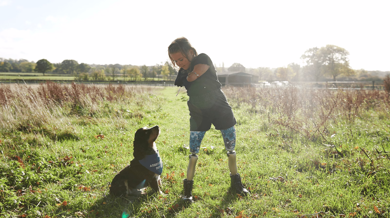 Bilateral Kenevo user Harmonie Rose Allen standing in a field next to her small black dog.
