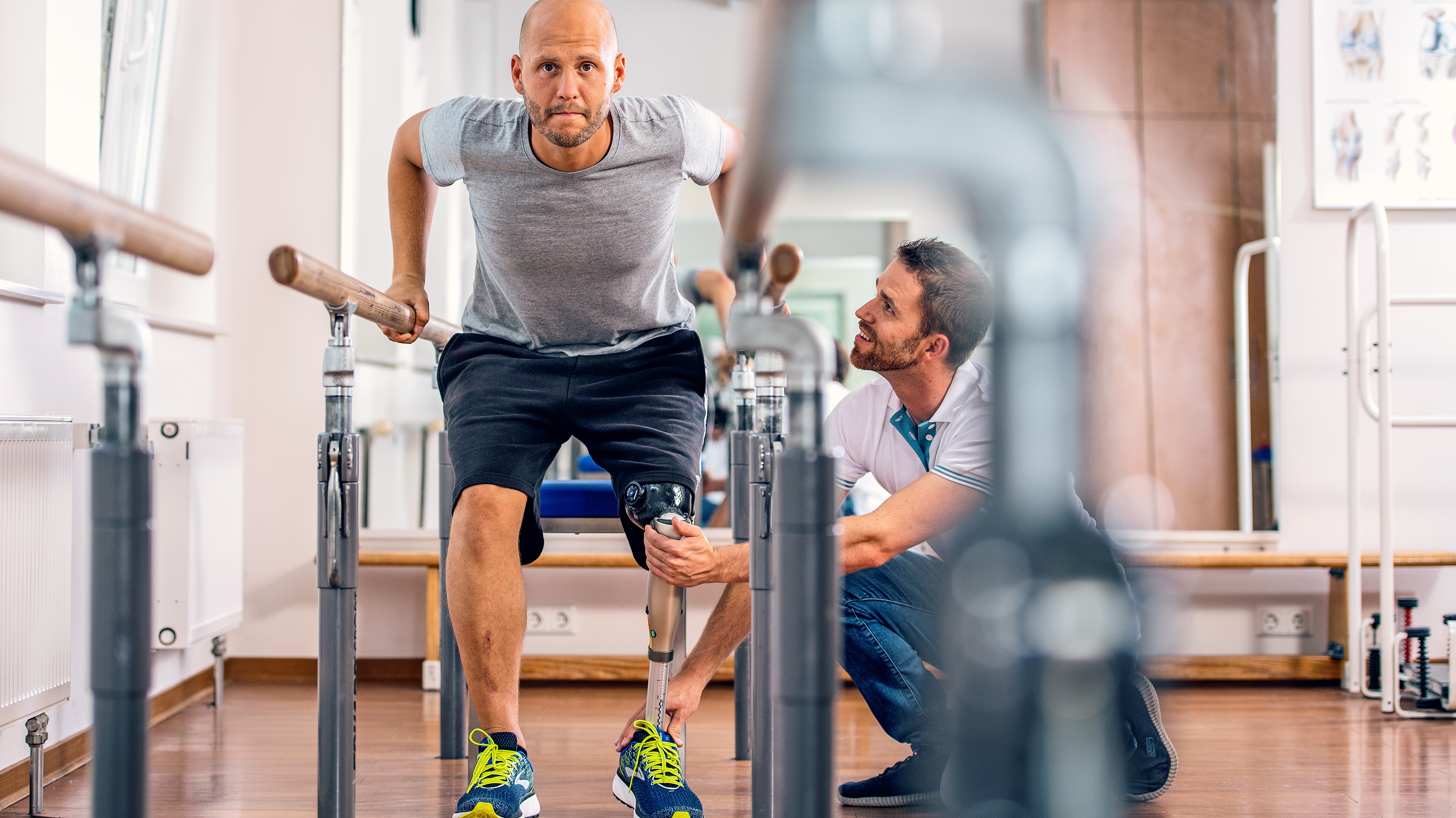 A man with a artificial knee squatting to test his prosthetic device while a Certified Prosthetist Orthotist (CPO) observes