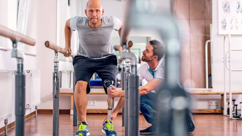 A man with a artificial knee squatting to test his prosthetic device while a Certified Prosthetist Orthotist (CPO) observes