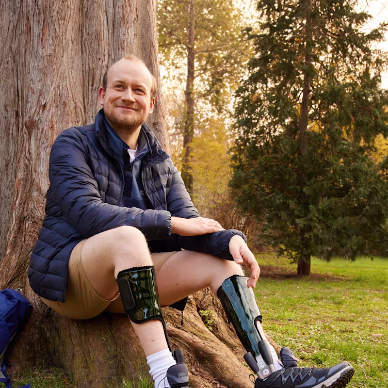 Auf dem Bild sieht man Domenic, der die Ottobock Tango Gelenke trägt und an einem Baum sitzt.