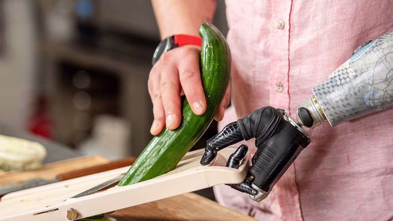 Ein Armprothesenträger schneidet in der Küche eine Gurke auf einem Brett. Er trägt eine bebionic Hand von Ottobock.