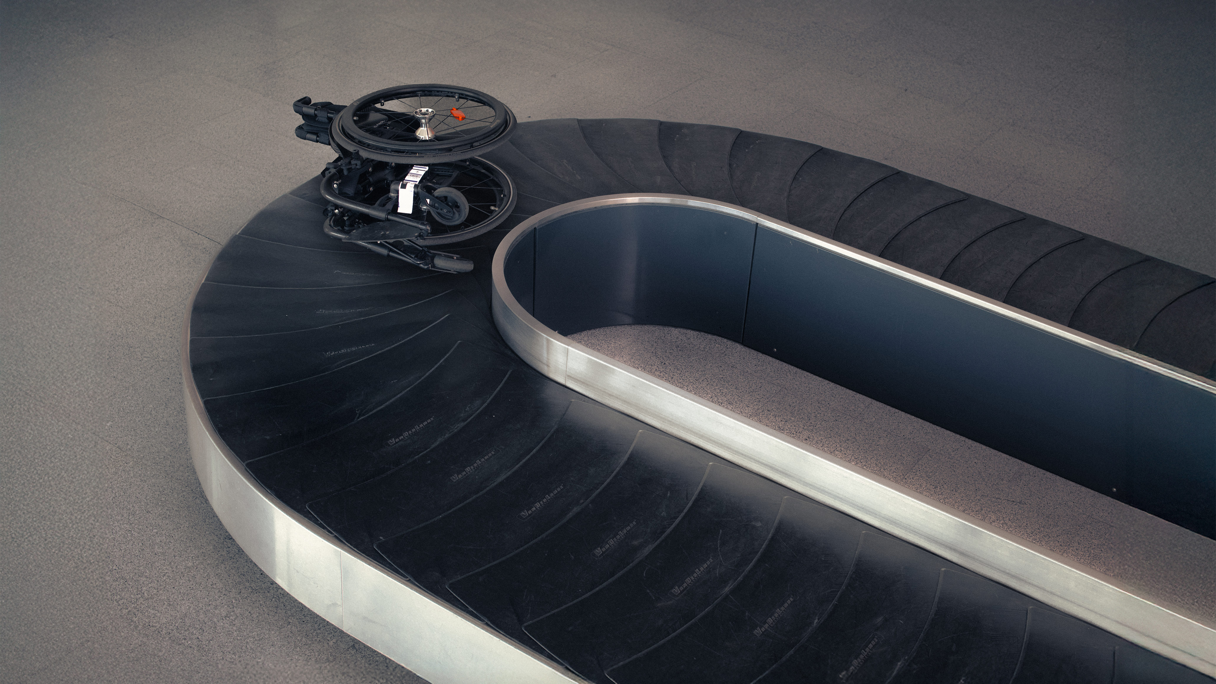 Wheelchair alone on an airport baggage carousel, illustrating the Invisible Class campaign message about lost and damaged mobility aids during travel.