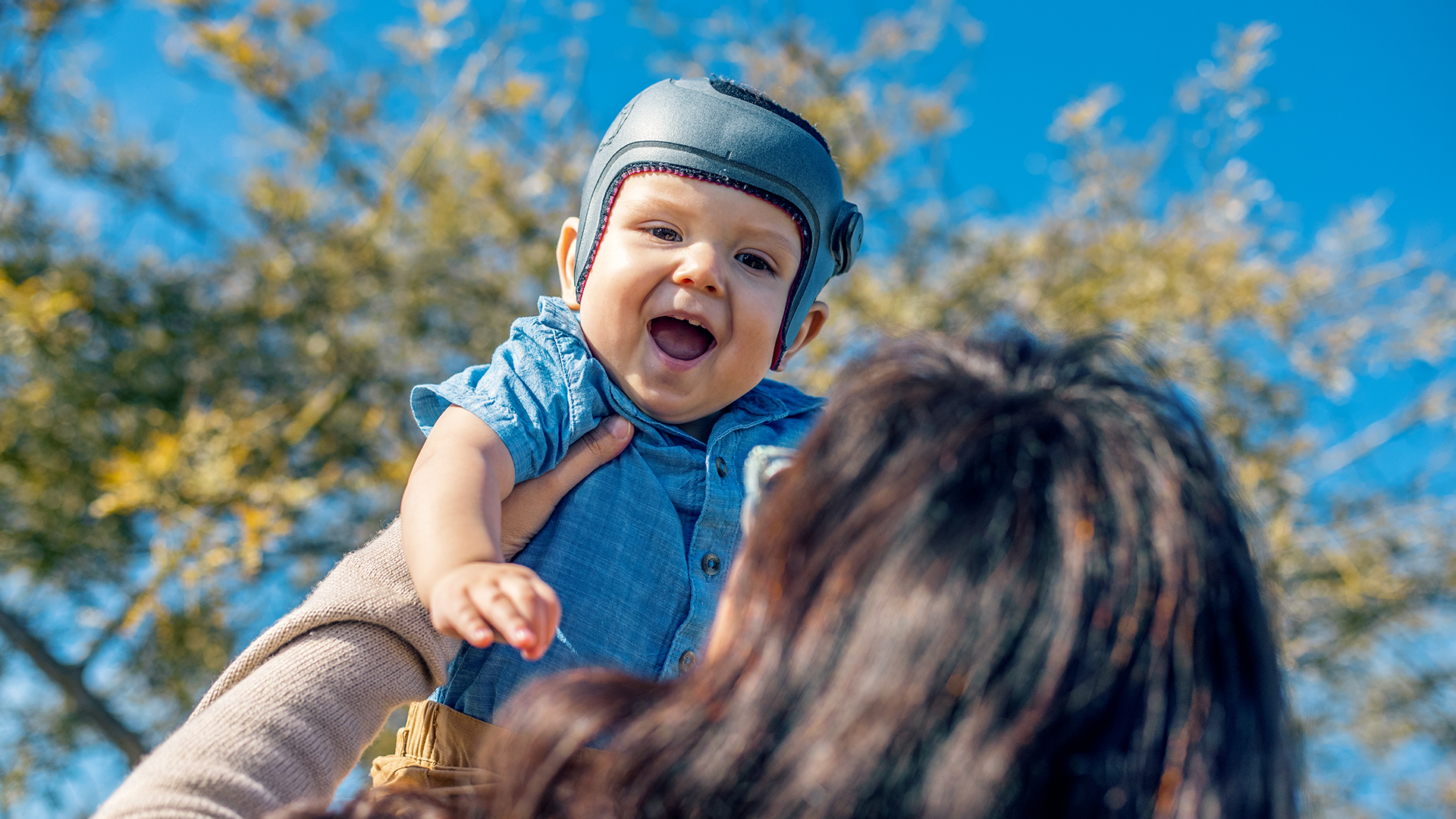 Harrison wears the MyCRO Band helmet, is lifted into the air and laughs.