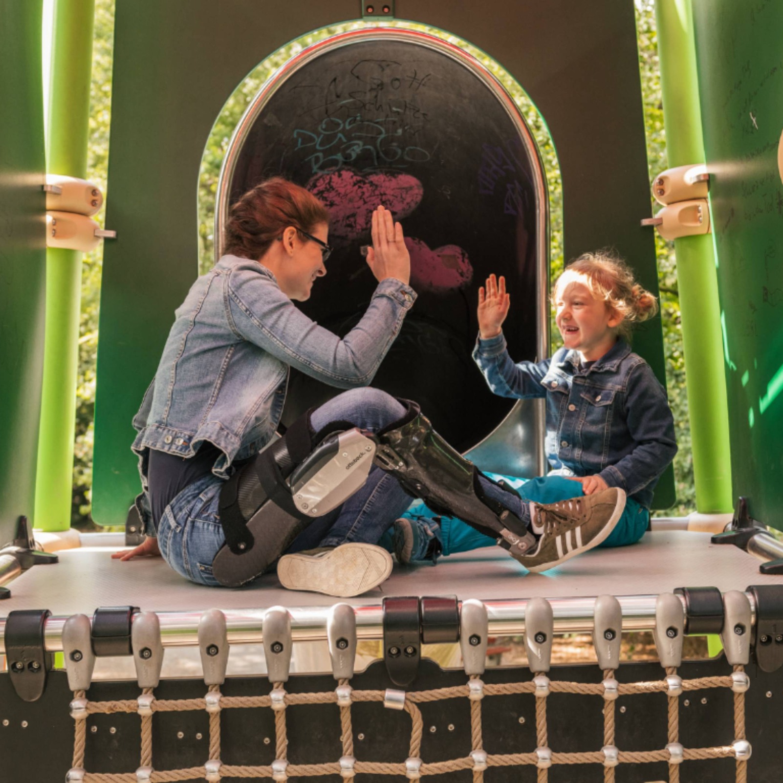 Une femme dans une C-Brace à l’intérieur d’un terrain de jeu d’enfant high-fiving son enfant