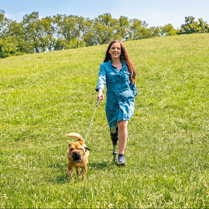 Un utilisateur de prothèse de membre inférieur marche son chien sur un champ