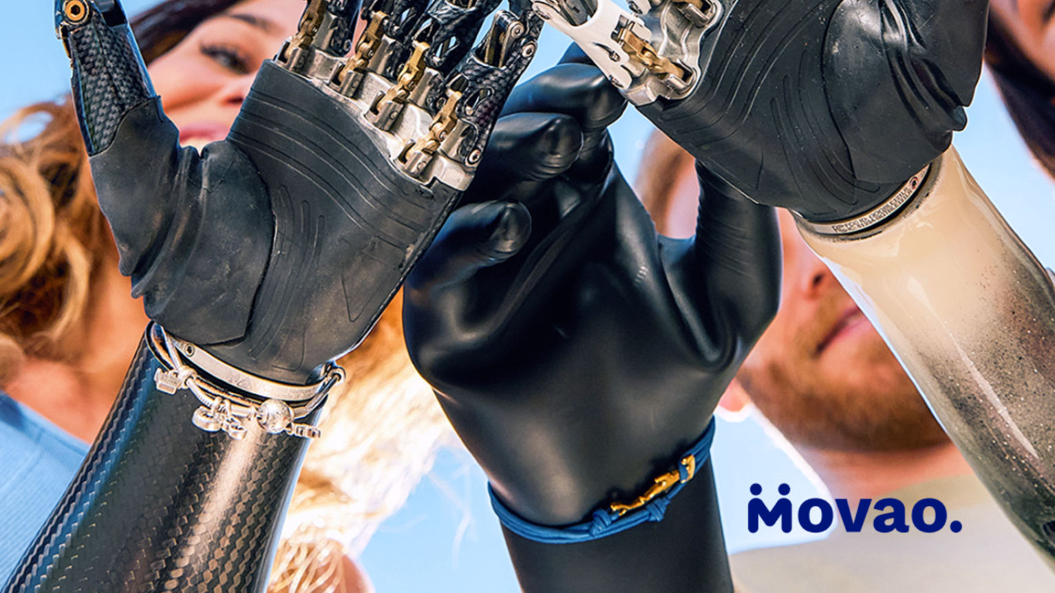 Groupe de personnes levant ensemble leurs bras et mains prothétiques Ottobock, symbolisant le soutien et la communauté – logo du réseau d'amputés Movao visible.