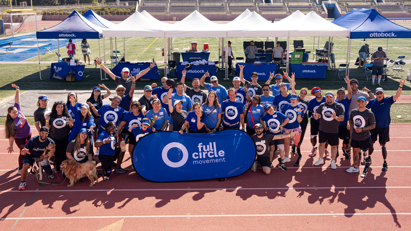 A large group of people standing on a running track on a sunny day gathered around a blue sign that says Full Circle Movement