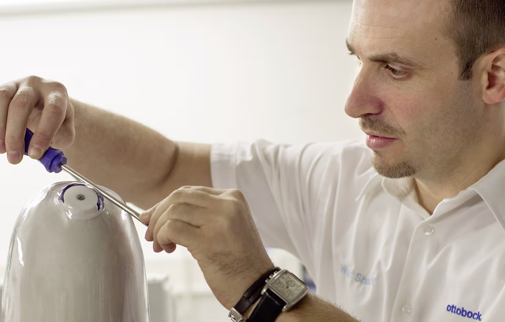 Ottobock technician assembling prosthetic limb using precision tools in workshop setting.