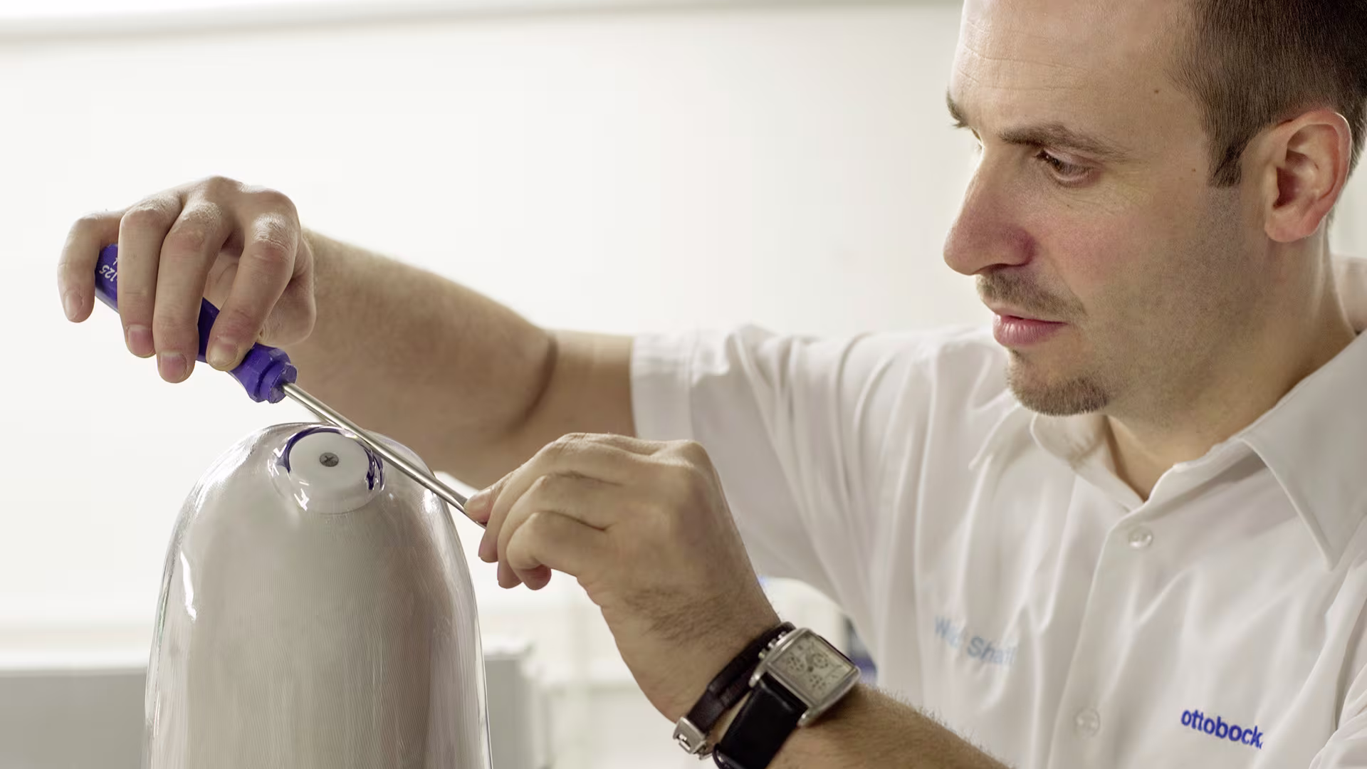 Ottobock technician assembling prosthetic limb using precision tools in workshop setting.