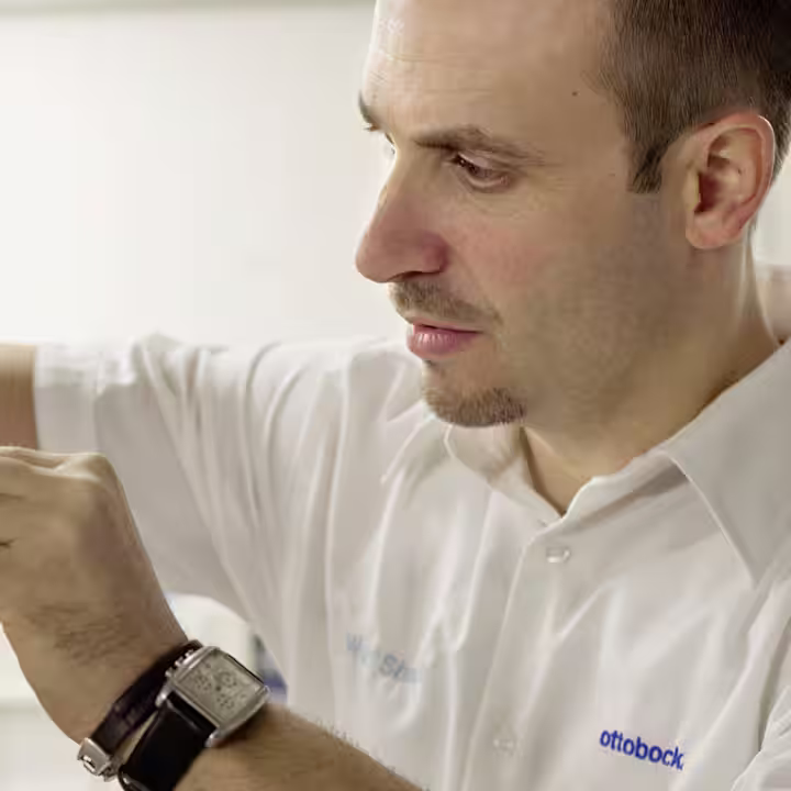 Ottobock technician assembling prosthetic limb using precision tools in workshop setting.