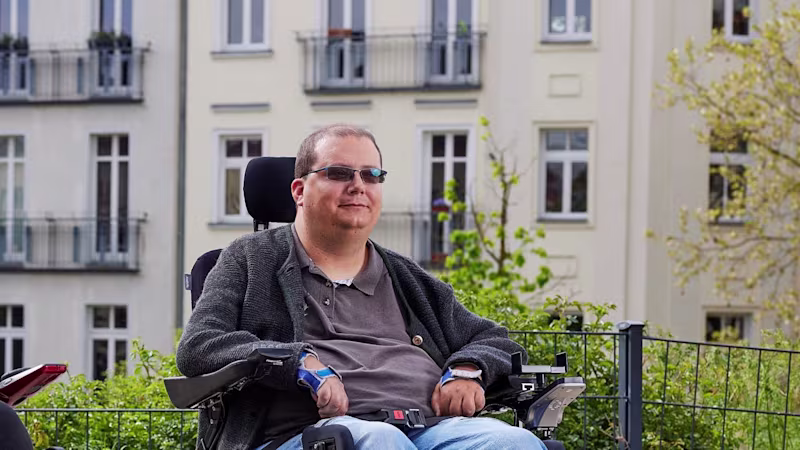 Akülü tekerlekli sandalye kullanıcısı Tobias, Ottobock Juvo B7'de, dışarıda Berlin'deki bir parkta dinleniyor ve güneşin tadını çıkarıyor.