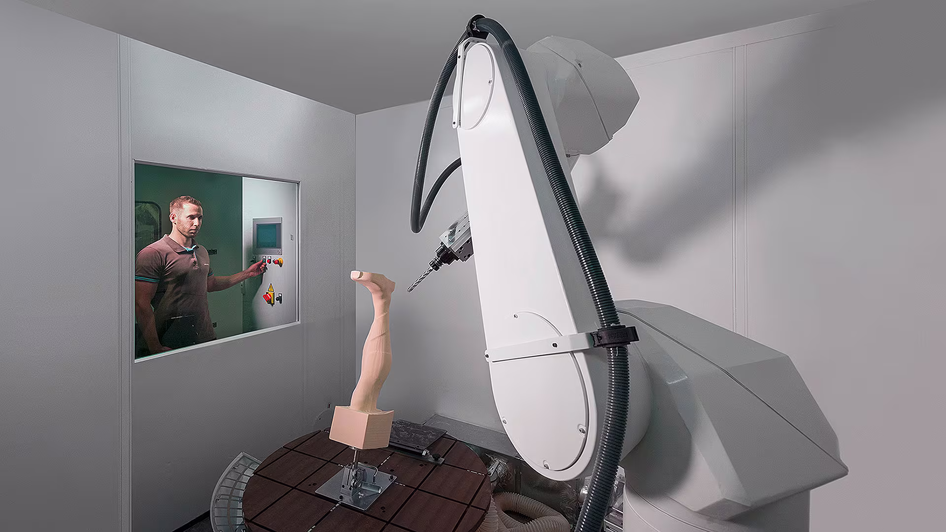 Robotic arm testing prosthetic leg model in Ottobock lab with technician monitoring through control window.