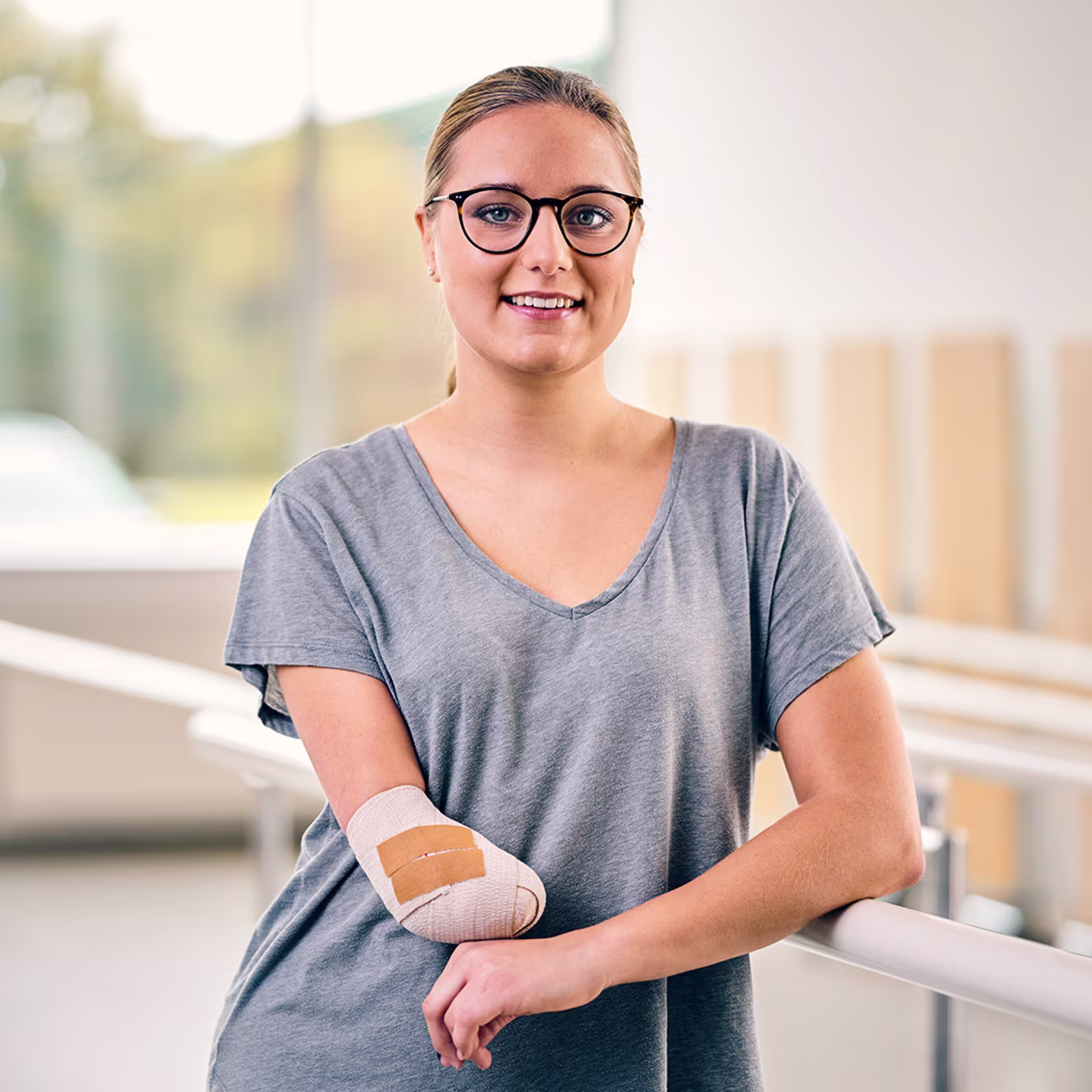 Portrait of a person wearing glasses in a bright indoor setting. The image represents rehabilitation after arm amputation and the journey toward restored mobility and independence.