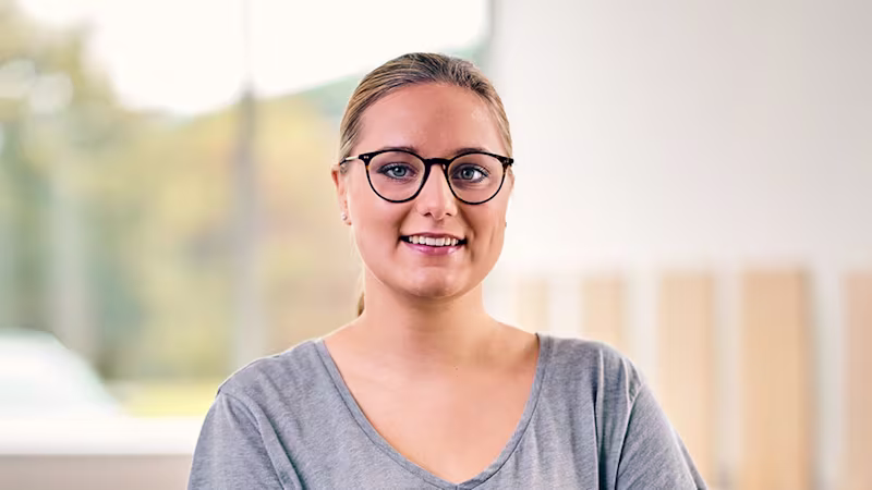 Portrait of a person wearing glasses in a bright indoor setting. The image represents rehabilitation after arm amputation and the journey toward restored mobility and independence.
