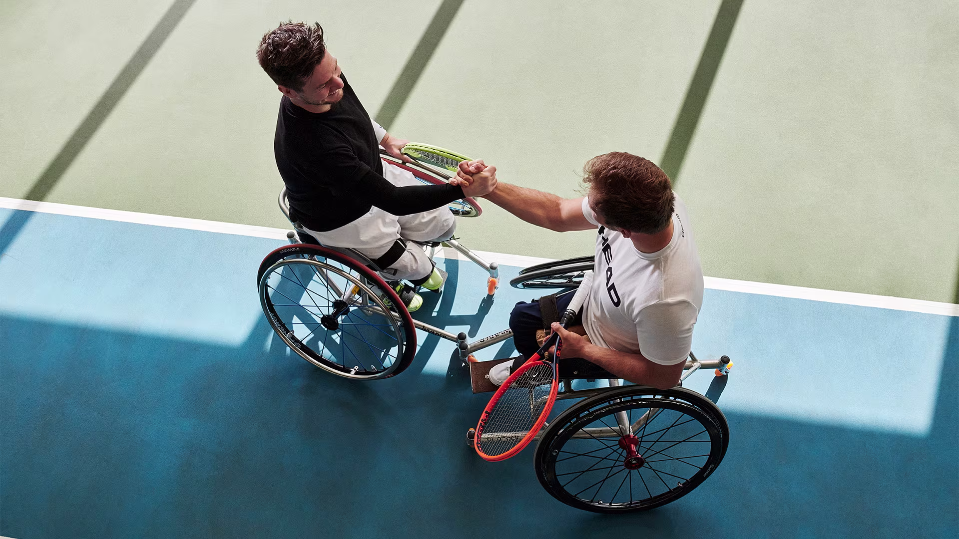 Two wheelchair tennis players shake hands on a tennis court
