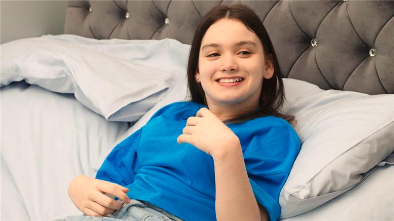 Ein junges Mädchen mit Zerebralparese liegt in einem Bett und lächelt.