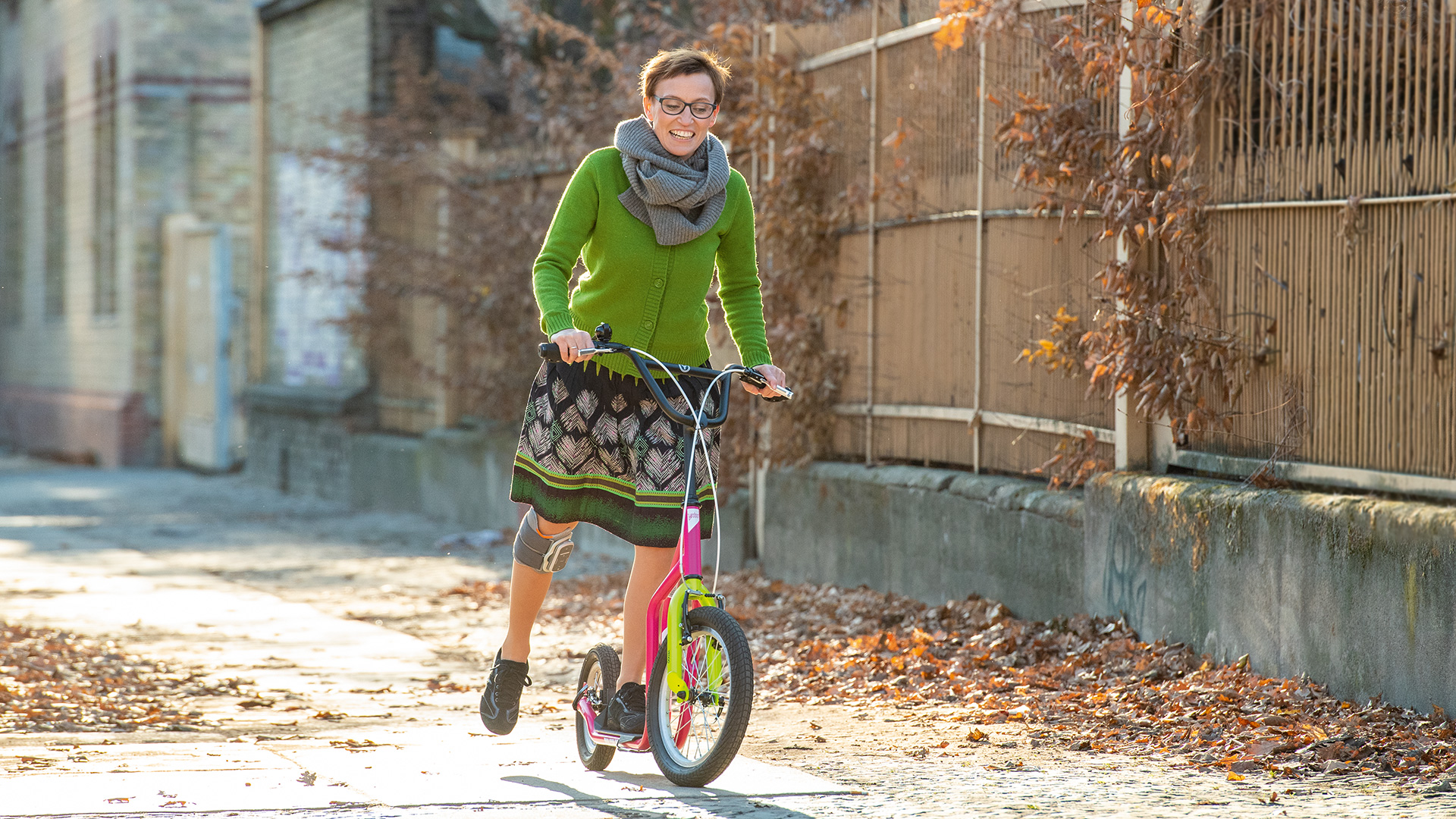 Eine weiblich gelesene Person trägt am rechten Bein das L100 Go von Ottobock. Sie steht auf einem bunten Roller, lächelt und gibt mit dem rechten Bein Anschwung.