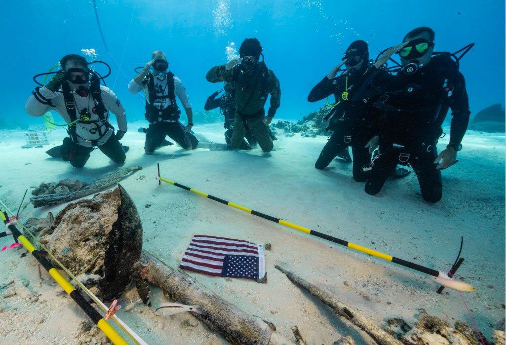Cinq plongeurs s'agenouillent sur le fond marin et saluent pour montrer leur appui à nos anciens combattants.