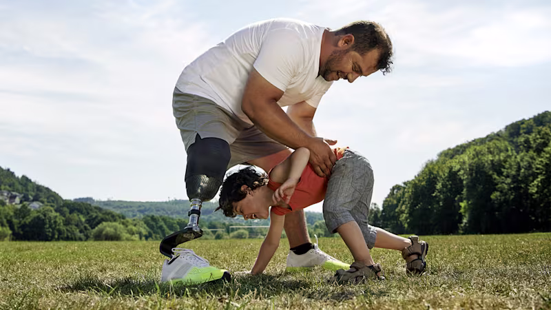 A person with a transtibial amputation plays with a child in a park.