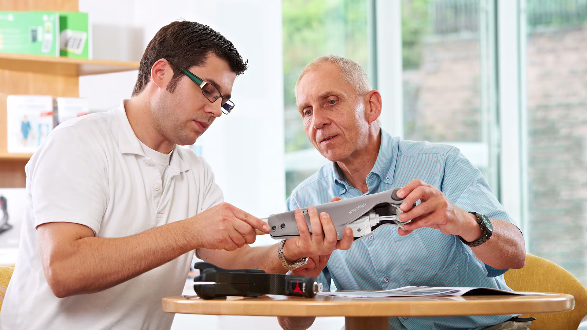 Zwei Orthopädietechniker, männlich gelesen, sitzen in der Werkstatt und arbeiten zusammen an einer Genium-Prothese von Ottobock. 