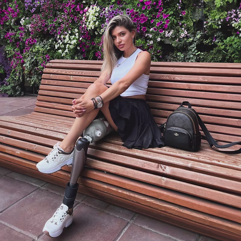 Девушка с протезом бедра с коленным модулем Genium сидит на скамейке в парке.