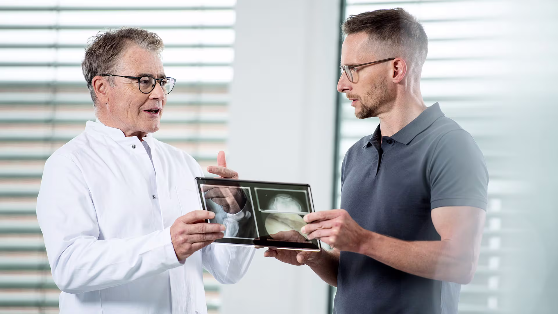 Ein Arzt zeigt einem jungen Mann Röntgenaufnahmen.