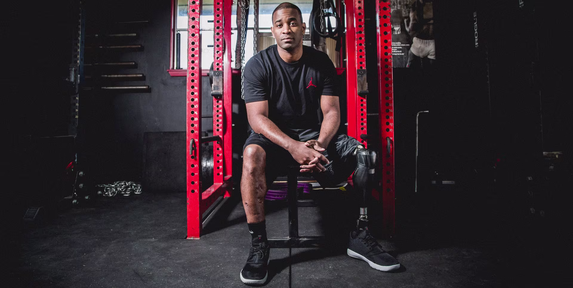 A male African American amputee veteran sits by his workout equipment and shows off his Ottobock prosthetic leg.