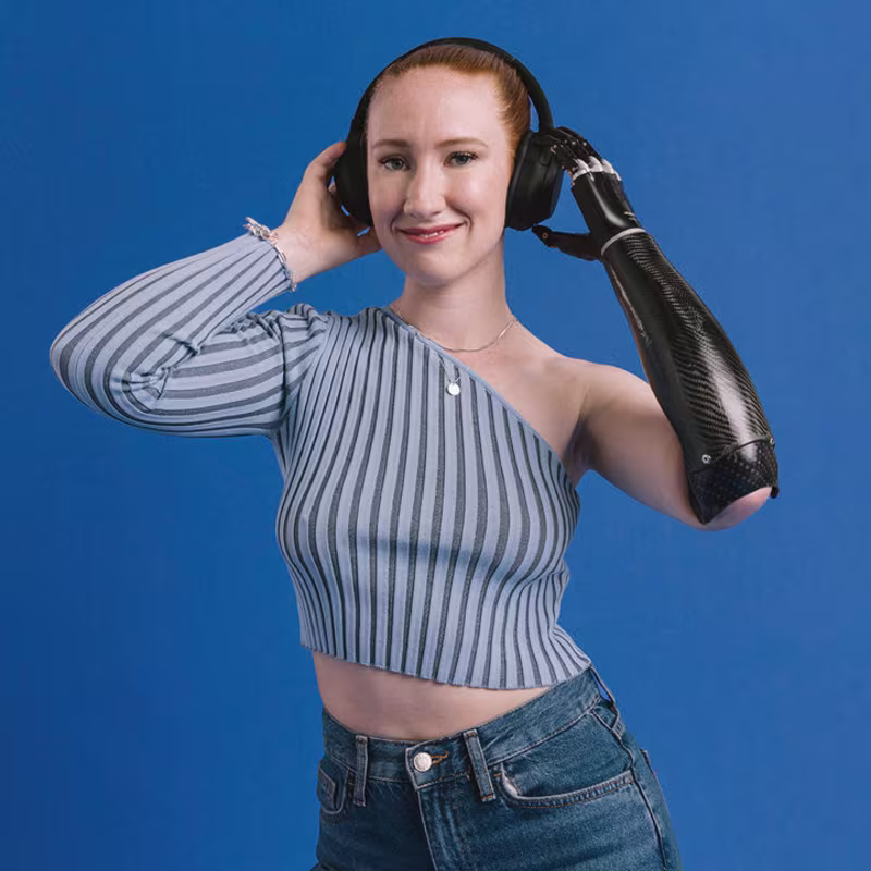 Eine Armprothesenträgerin hört Musik und hält Ihre Hände an den Kopfhörern. Sie trägt die bebionic Hand von Ottobock.