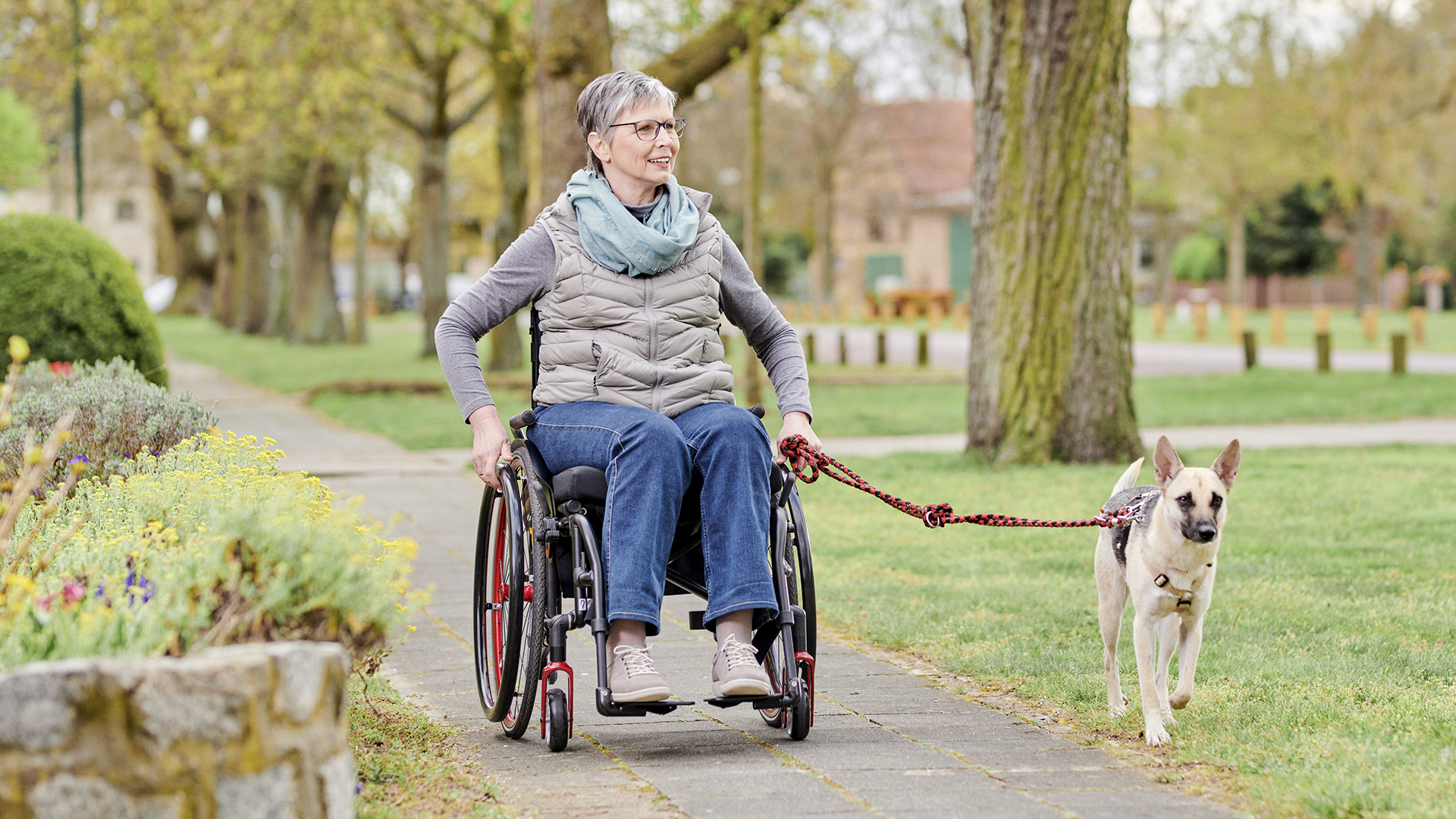Wanda in her red Ottobock Avantgarde wheelchair walking her dog in a park.