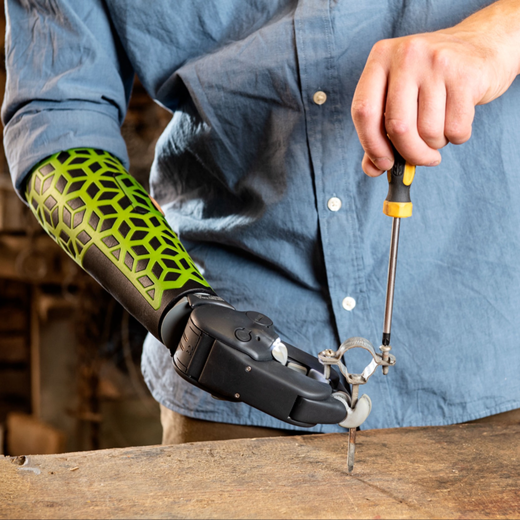 A myoelectric prosthetic hand user holding a nail while using a screwdriver with their biological hand 