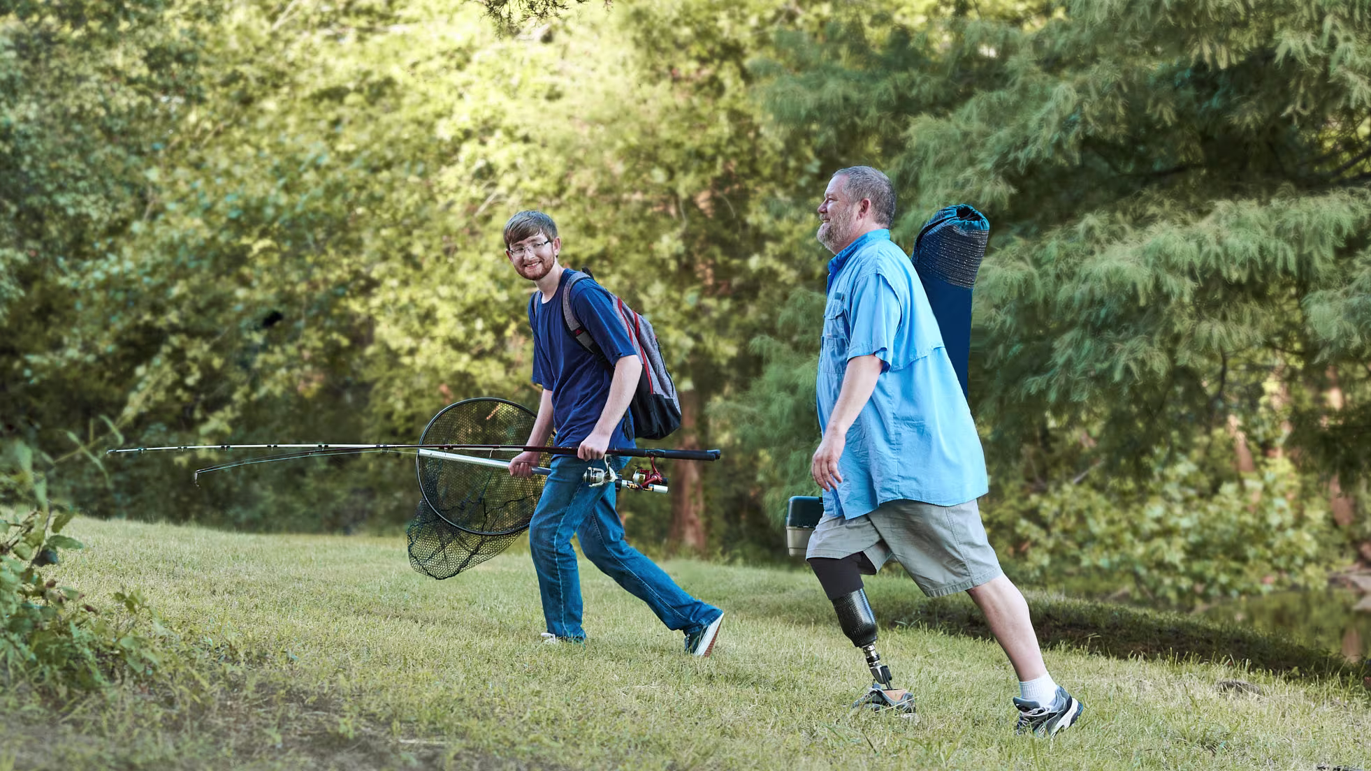 Two men transport various fishing equipment through a forest. The man in the forefront of the photo sports the custom Ottobock Taleo bionic foot on his right leg.