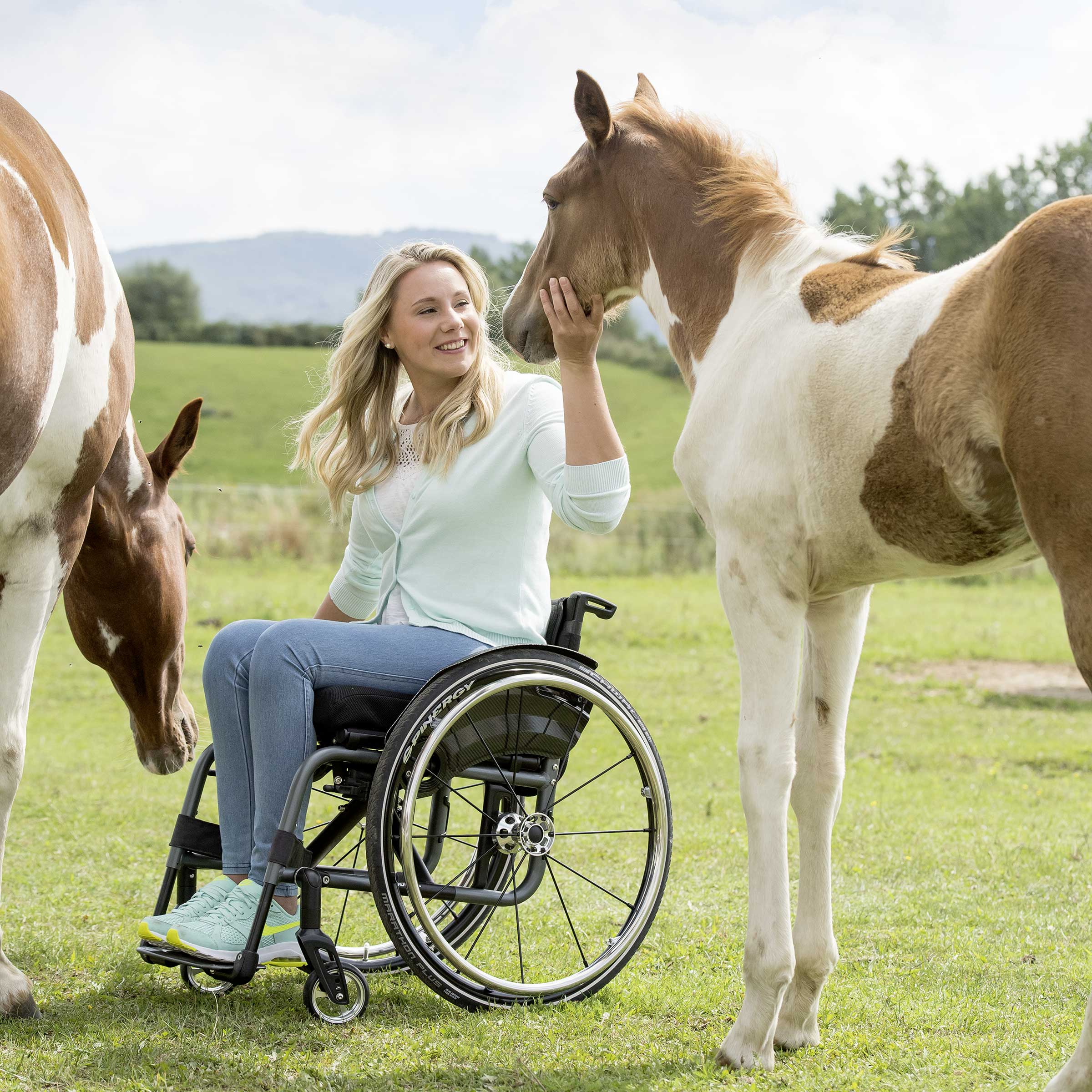 Svenja sitting in her Avantgarde 4 manual wheelchair from ottobock petting a horse's head. 