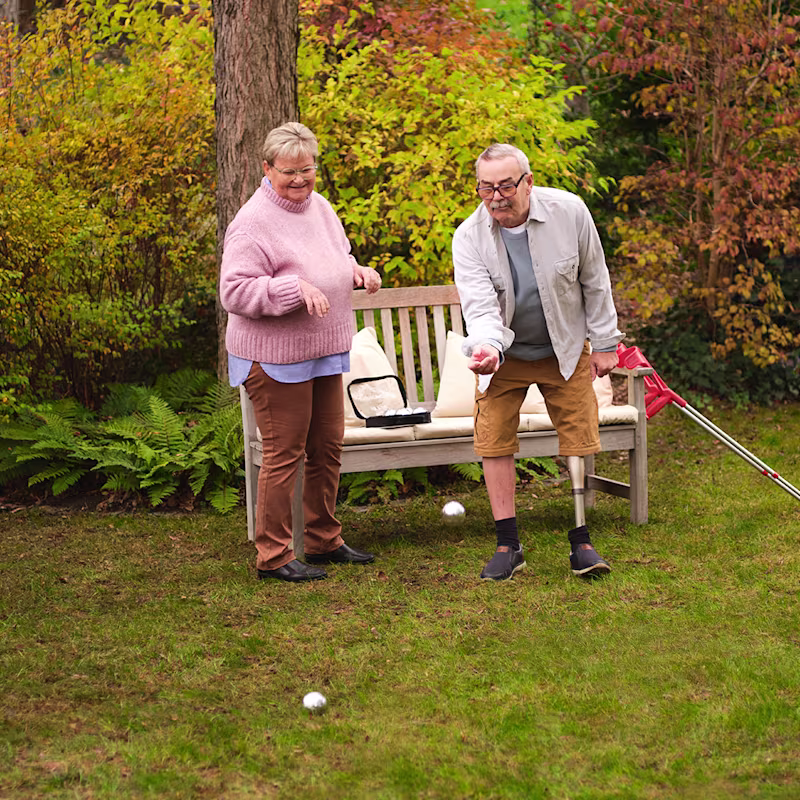 Ein älteres Paar spielt gemeinsam im Garten Boule. Der Mann trägt dabei das mechatronische Kniegelenk Kenevo von Ottobock.
