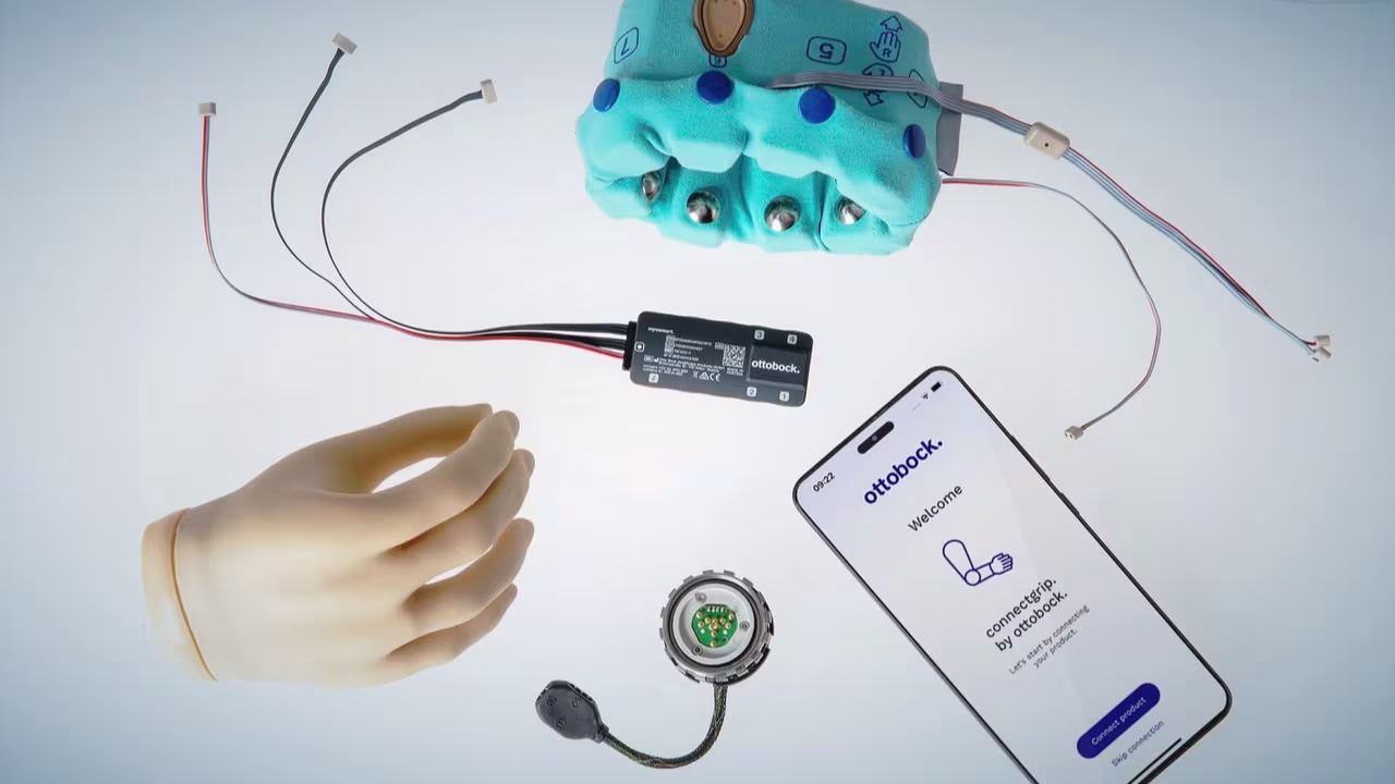 Upper limb extremity components on a brightly lit white background, including a phone displaying the ottobock connectgrip app, ottobock speedhand, and ottobock myosmart cuff