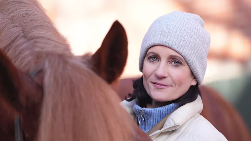 Siglind steht mit Ihrem Pferd vor Ihrem Pferdestall. Sie trägt das mechatronische Prothesenkniegelenk Genium X4 von Ottobock.