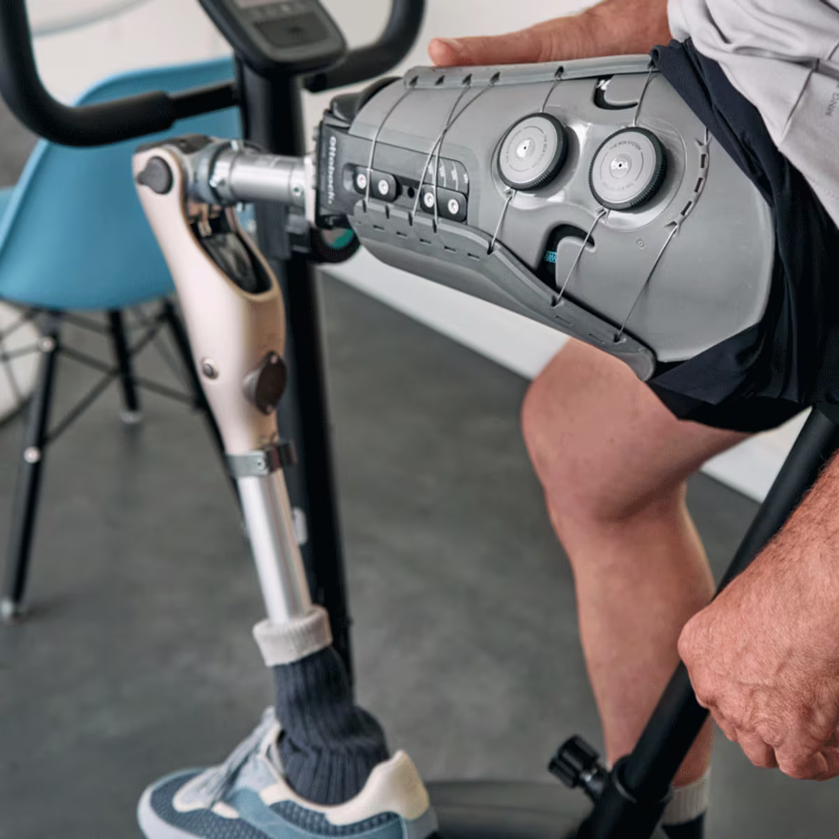 Plan rapproché d’un homme assis sur une bicyclette couchée dans un cadre clinique avec un pied prothétique, un genou et une combinaison douille/manchon. le genou est un genou à microprocesseur Ottobock Kenevo et la douille est une douille à volume réglable Ottobock Varos.