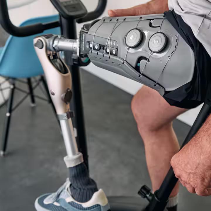 Plan rapproché d’un homme assis sur une bicyclette couchée dans un cadre clinique avec un pied prothétique, un genou et une combinaison douille/manchon. le genou est un genou à microprocesseur Ottobock Kenevo et la douille est une douille à volume réglable Ottobock Varos.