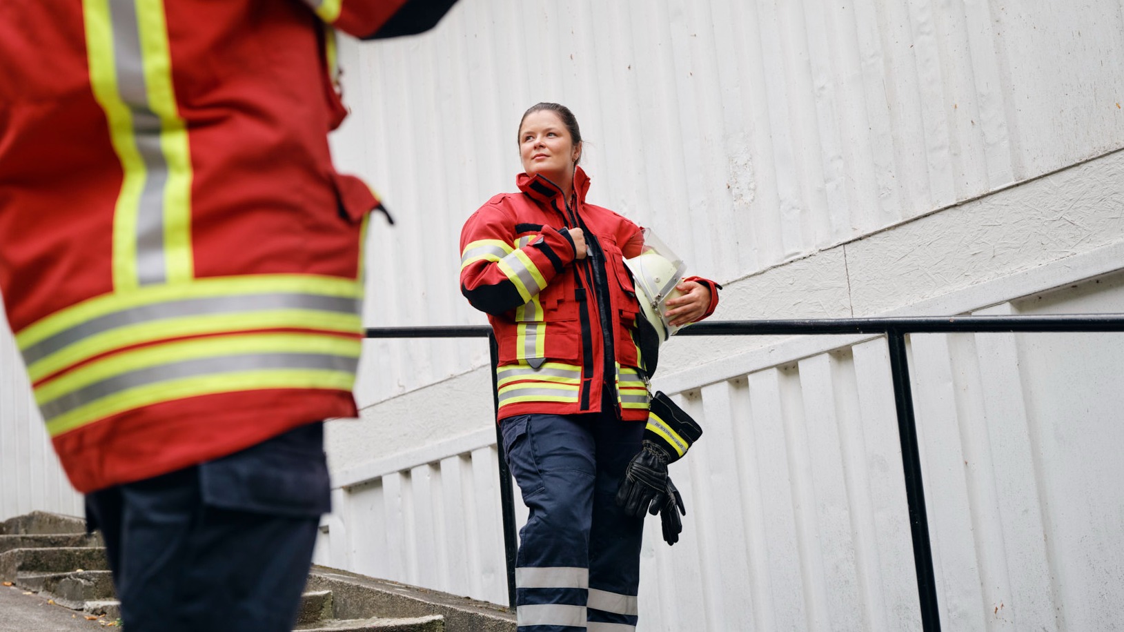 Firefighter Lena stands confidently on outdoor stairs in her red and yellow uniform, representing courage, teamwork, and dedication.