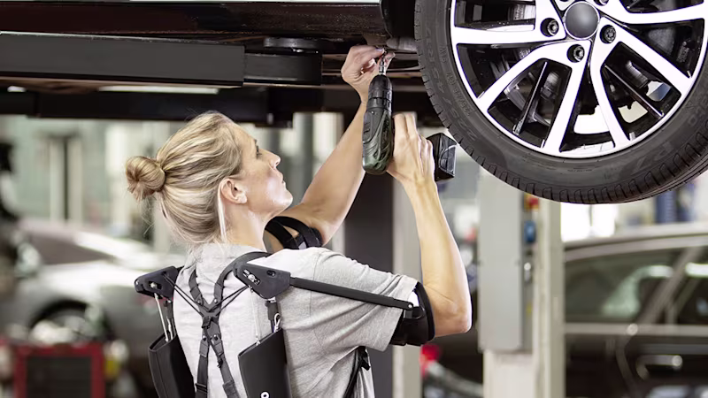 Eine Arbeiterin in der Automobilproduktion arbeitet über Kopf mit dem Paexo Exoskelett ohne ihren Rücken zu arg zu belasten.
