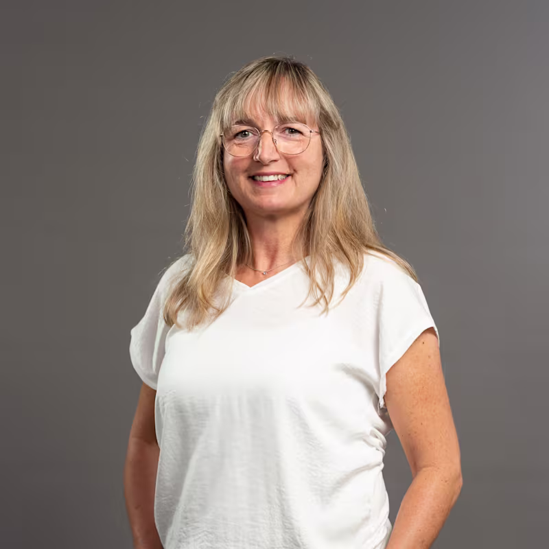 Auf dem Bild ist das Portrait einer Ottobock Academy Mitarbeiterin zu sehen. Sie hat blonde lange Haare, trägt eine Brille und lacht in die Kamera.