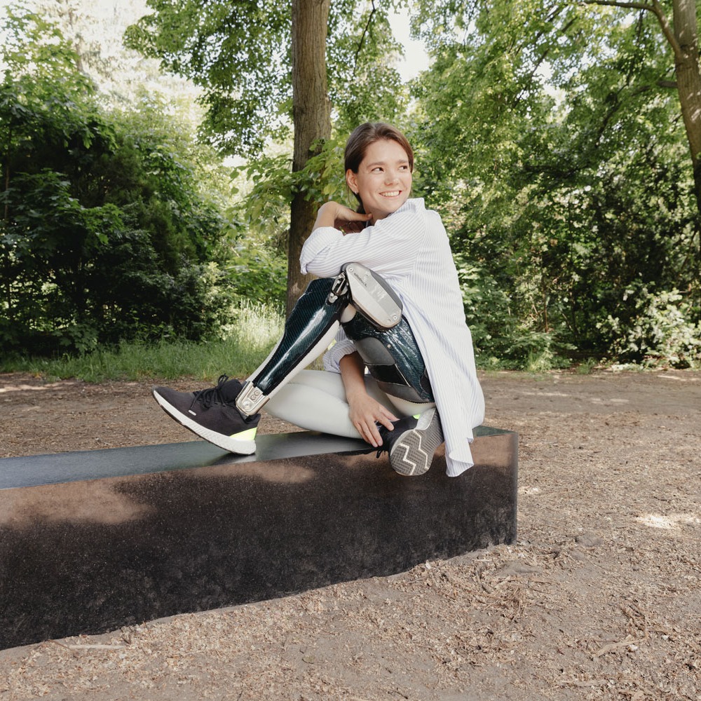 An Ottobock C-Brace user sitting on a bench in a park