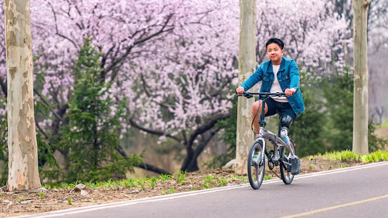 A teenage boy rides a bicycle in a park, wearing a prosthetic leg.