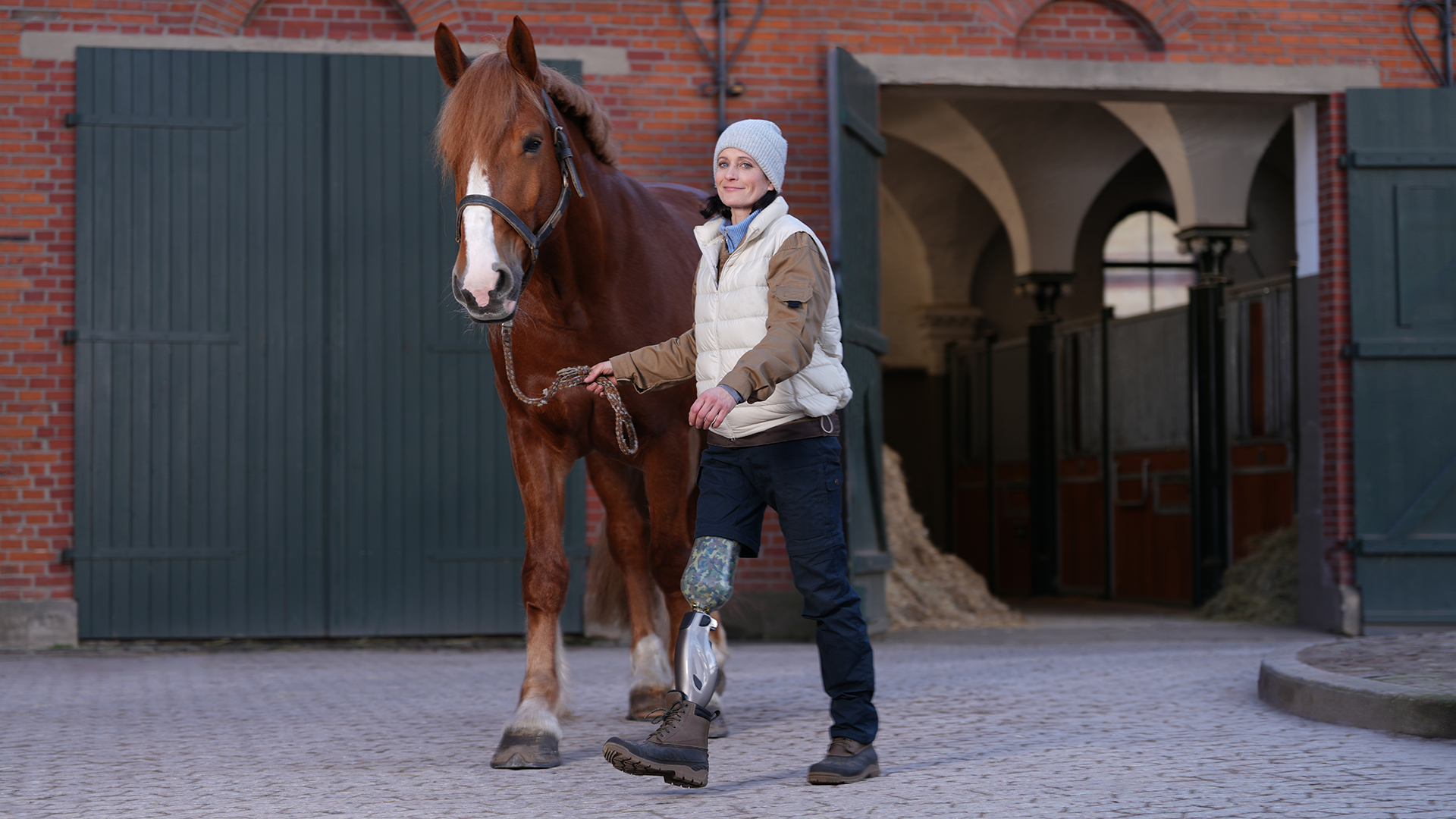 Die Prothesenträgerin Siglind führt ihr Pferd über den Hof. Sie trägt dabei das Genium X4 von Ottobock.