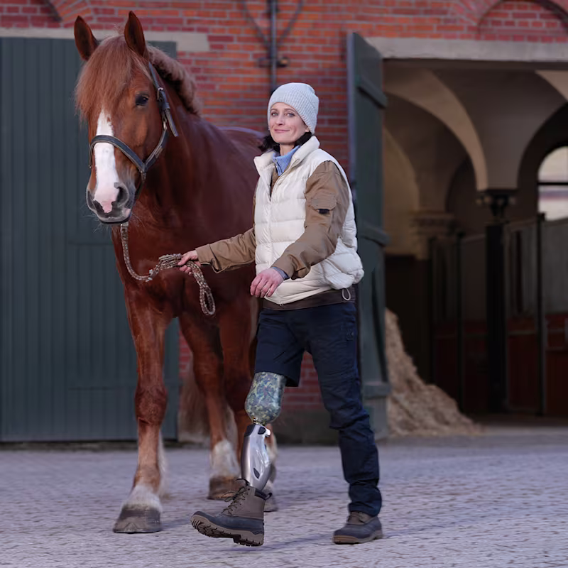 Die Prothesenträgerin Siglind führt ihr Pferd über den Hof. Sie trägt dabei das Genium X4 von Ottobock.
