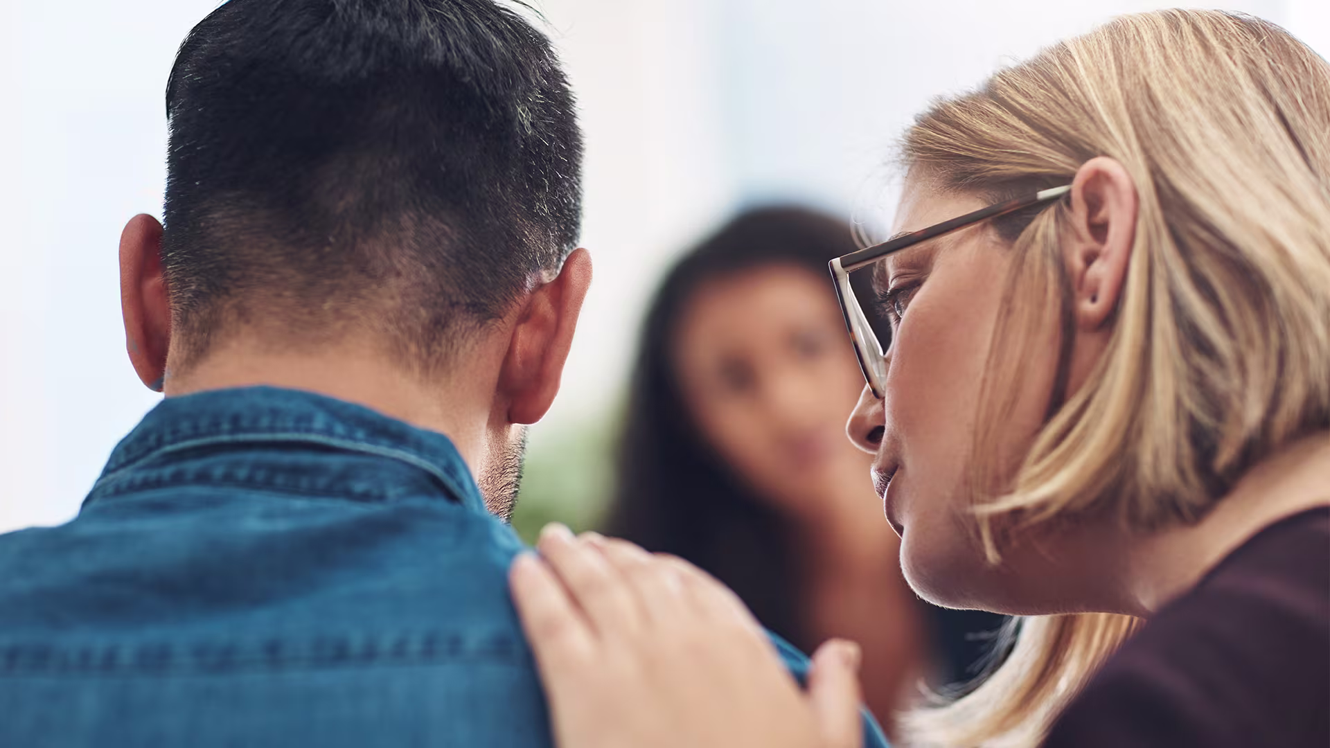 Eine Frau und ein Mann sind im Profil zu sehen und unterhalten sich. die Frau legt dabei unterstützend ihre Hand auf die Schulter des Mannes.
