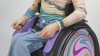 Nahaufnahme von Nomine in ihrem lilafarbenen kidevo mini.t Rollstuhl von Ottobock mit Gurt.