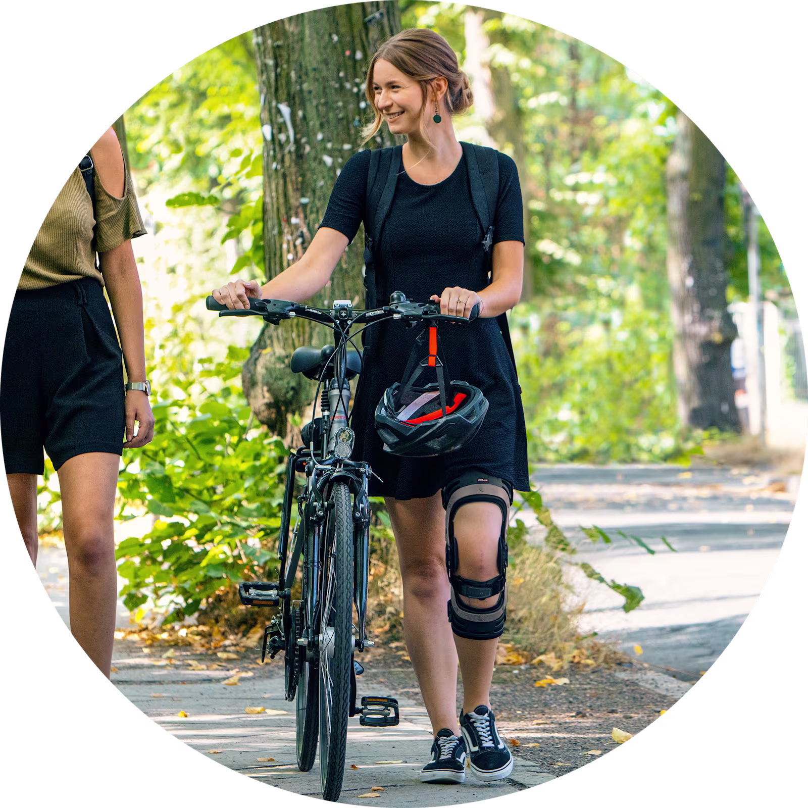 Zwei weiblich gelesene Personen gehen in der Stadt spazieren. Die rechte Person schiebt ihr Fahrrad, dabei trägt Sie eine Genu Arexa von Ottobock.