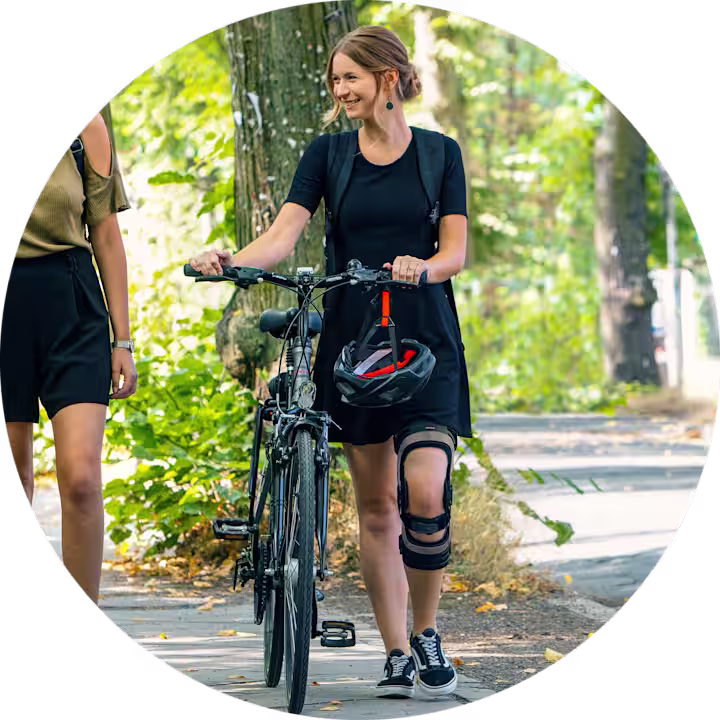 Zwei weiblich gelesene Personen gehen in der Stadt spazieren. Die rechte Person schiebt ihr Fahrrad, dabei trägt Sie eine Genu Arexa von Ottobock.