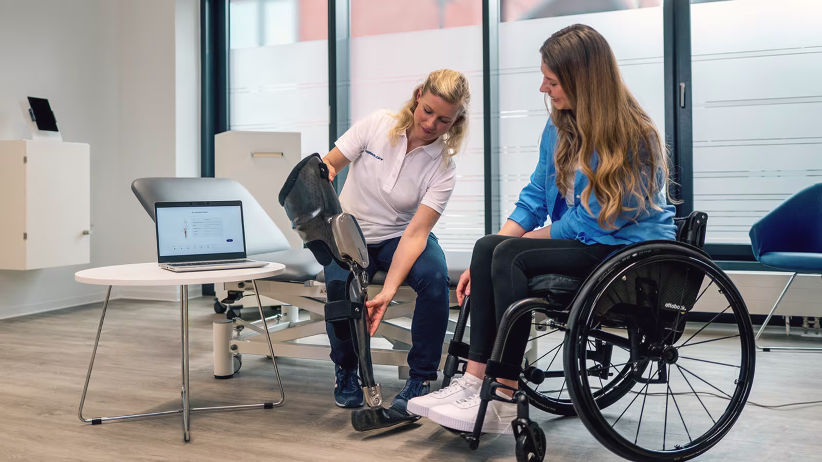 In einem Versorgungszentrum sitzt eine Anwenderin im Rollstuhl, während ihr von einer Mitarbeiterin das C-Brace, ein modernes Orthesen System, vorgestellt wird.