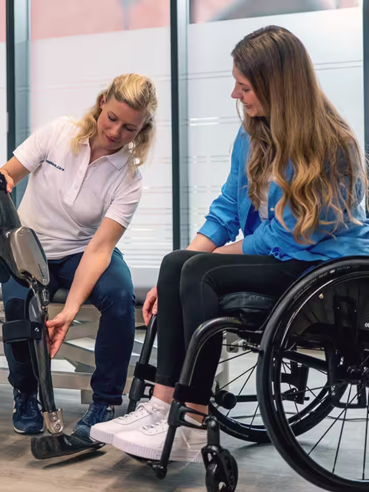 In einem Versorgungszentrum sitzt eine Anwenderin im Rollstuhl, während ihr von einer Mitarbeiterin das C-Brace, ein modernes Orthesen System, vorgestellt wird.
